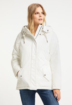 Frau trägt eine weiße Winterjacke mit Kapuze, Kordelzügen und Taschen, kombiniert mit blauen Jeans, und blickt leicht zur Seite.