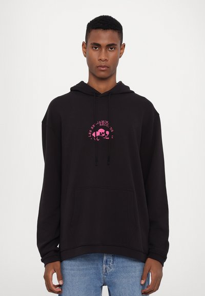 Black hooded sweatshirt with pink graphic print featuring a skull and text. Kangaroo pocket and drawstring hood. Casual fit.