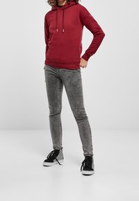 Bordo mikina s kapucí na šňůrku, nošená s přiléhavými šedými džíny, doplněná černo-bílými kostkovanými sneakers na vysoké podešvi.