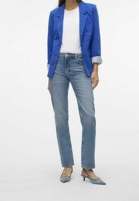 Niebieska marynarka na biały shirt, zestawiona z jasnoniebieskimi prostymi spodniami jeansowymi i niebieskimi butami na obcasie typu slingback. Marynarka ma podwinięte mankiety i kieszenie.