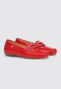 Par de mocasines loafers de piel roja con detalle de pieza metálica y suelas de goma marrón sobre un fondo gris claro.