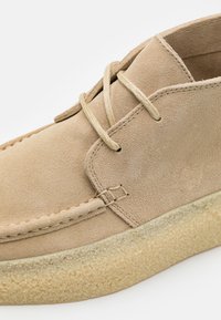 Chaussure décontractée en suède beige avec lacets beiges, couture détaillée et semelle en caoutchouc crêpé texturée.