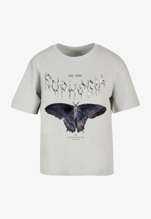 Helehall puuvillane T-särk ringsuutsega. Sellel on suur must jahall liblikalogo ning stiliseeritud tekst nende kohal ja all.