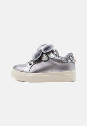 Sneaker grigio metallico per bambini con accenti argento, grande fiocco di velluto grigio sui lacci, toppa glitterata sul tallone e suola beige.
