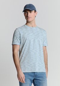 Lichtblauw T-shirt met korte mouwen, voorzien van horizontale strepen in verschillende tinten. Zachte stof, ronde halslijn, gecombineerd met een blauwe pet en denim jeans.