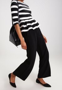 Haut peplum rayé noir et blanc avec des manches trois-quarts, associé à un pantalon noir à jambes larges et des ballerines noires pointues. Sac à main noir inclus.