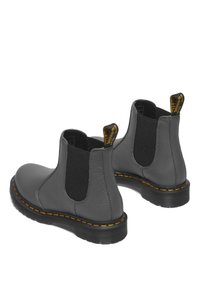 Botas Chelsea de cuero gris con paneles laterales elásticos, suelas negras y costuras amarillas. Presentan una lengüeta para facilitar el calzado.