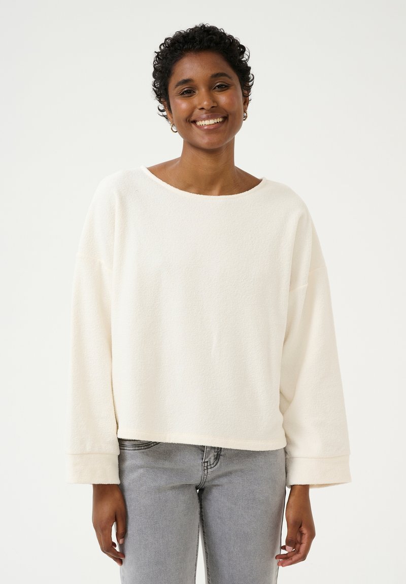 Fleece Sweatshirt mit Rundhalsausschnitt in Creme, mit lockerem Schnitt, weitem Ausschnitt und umgeschlagenen Bündchen, kombiniert mit hellgrauen Jeans.