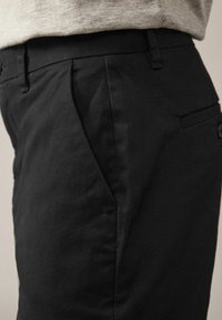Pantaloni negri dintr-un material texturat, cu un buzunar lateral, față plisată și un design slim fit.