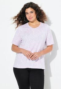 Camiseta de manga corta de color púrpura claro con un patrón de líneas abstractas blancas, cuello redondo y un corte holgado, combinada con pantalones negros.