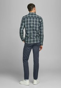 Groen en marineblauw geruit overhemd met een button-down kraag, gecombineerd met donkergrijze broek en witte sneakers. Achteraanzicht toont de slanke pasvorm en ontwerprichtlijnen.