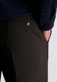 Bruine geprinte broek met een gladde textuur en een enkele knoopsluiting op de tailleband, gecombineerd met een donkerblauwe overhemd met knopen aan de mouwen.