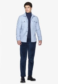 Lys blå skjortejakke i uldblanding med to brystlommer, parret med en navy turtleneck og navy cord-jersey bukser. Sorte slipsko fuldender outfittet.