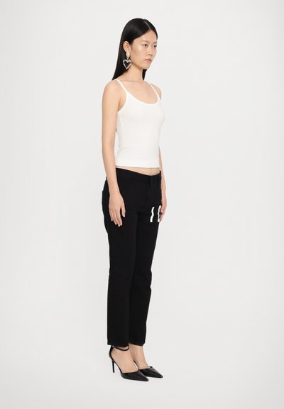 Witte, strakke tanktop; zwarte, taps toelopende broek met een witte grafische print. Model draagt zwarte hoge hakken en is geaccessoriseerd met grote hartvormige oorbellen.