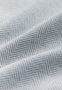 Tissu textile présentant un motif en chevrons dans des nuances de gris, avec une texture douce et un léger éclat, affichant une profondeur subtile dans le design.