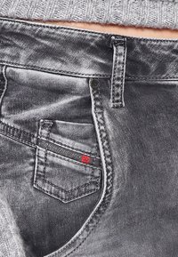 Gray denim jeans with a front pocket featuring a small red accent tag. The fabric has a smooth texture and subtle fading.