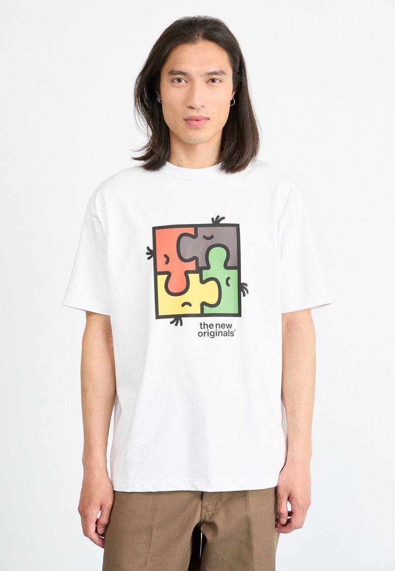 Weißes Baumwoll-T-Shirt mit einem bunten Puzzle-Design (orange, grün, grau, gelb) und cartoonartigen Gesichtern sowie dem Text „the new originals“. 