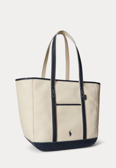 Kremfarvet canvas tote taske med navyblå læderkant, lange håndtag, frontlomme og lille broderet polo-spiller logo.