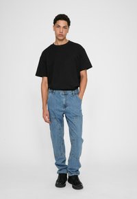 Black cotton T-shirt with short sleeves, paired with light blue denim jeans featuring patch detailing and stitched accents. Black sneakers.