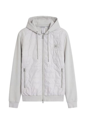 Chaqueta gris claro con capucha, parte delantera acolchada, dos bolsillos con cremallera, cremallera completa en el frente y capucha con cordón ajustable.