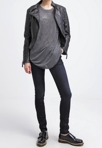 Svart läderbikerjacka med texturerade axlar, grå grafisk t-shirt med metalliska nitar, mörka skinny jeans och svarta skor med gummisula.