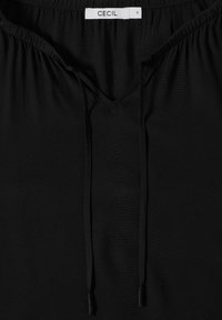 Blusa nera con scollatura a V, realizzata in materiale morbido. Presenta dettagli con cordoncino sul colletto e arricciature elastiche intorno alle spalle.