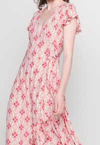 Rosa Wickelkleid mit floralem Muster, kurzen Rüschenärmeln, gemustertem Stoff und einer gebundenen Taillendetail. Leichter Stoff mit fließender Passform.