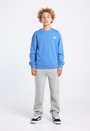 Blauwe sweatshirt met geribbelde manchetten en zoom, gecombineerd met grijze trainingsbroek met zijstrepen en zwarte sneakers. Simpele, ontspannen pasvorm.