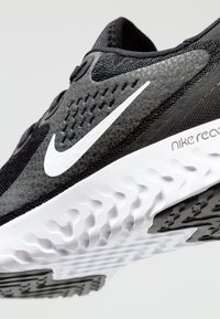 Chaussure de course Nike noire et blanche avec semelle texturée, swoosh Nike visible sur le côté, et marquage "nike react" près du talon.