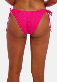Hot pink hæklede bikinitrusser med geometriske mønstre, sidebånd der har små guldperler. Struktureret finish, lavt skåret design.