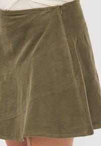 Olijfgroene corduroy rok met een flare-vorm, zichtbare stiksels en een zijrits. Heeft een gestructureerd, ribbelig oppervlak.