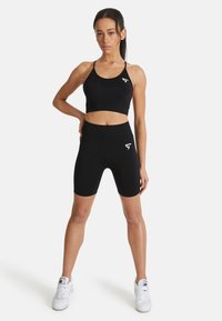 Zwarte sportkledingset met een cropped tanktop en high-waisted fietsbroek, gemaakt van rekbare stof met een gladde textuur, met logo detail.