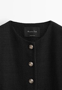 Svart texturerad jacka med rund halsringning och fyra glänsande guldknappar framtill; varumärkesetiketten läser "Massimo Dutti."