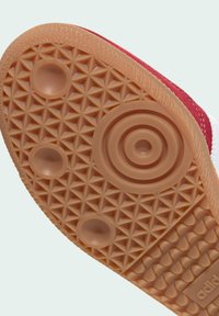 Semelle en caoutchouc marron avec des motifs de bande de roulement circulaires et triangulaires sous une basket rouge et blanche.