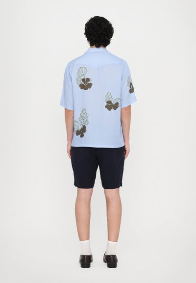 Lys blå kortermet skjorte med blomsterprint i mørkebrunt og grønt. Bært med mørke shorts, hvite sokker og brune sko.