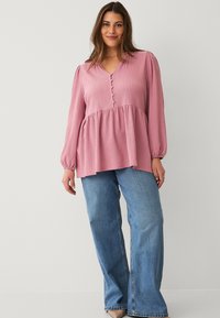 Pink textured blouse with a V-neck, long sleeves, and front button details, paired with light blue wide-leg jeans.