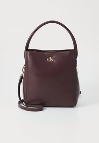 Bordeaux leren handtas met een gladde textuur, voorzien van een gouden "CK" logo, een korte handgreep en een afneembare schouderriem.