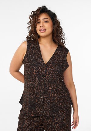 Woman wearing sleeveless leopard-print button-up top matching leopard-print pants, standing with one hand behind her back.
