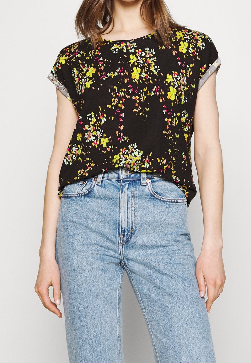 Czarny krótki top z rękawem, z kwiatowym wzorem w żółtym, różowym i zielonym kolorze. Luźny krój, okrągły dekolt i mankiety z tkaniny. Połączony z jasnoniebieskimi dżinsami.