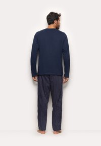 Mørkeblå langærmet skjorte lavet af blødt stof, parret med marineblå og hvide stribede pyjamasbukser. Lige snit med ribbet tekstur.