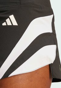 Svart sportkjol med vita accentpaneler, design med tre ränder och Adidas-logotyp. Slät textur med en sydd fåll.