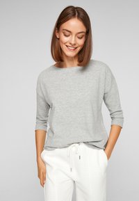 Lichtgrijze long-sleeve top met een ronde halslijn en een losse pasvorm, gecombineerd met gestructureerde witte broeken met een trekkoorddetail.