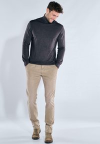 Dark gray turtleneck sweater, beige chinos, and brown ankle boots, featuring a slim fit and smooth texture. Casual attire with a relaxed posture.