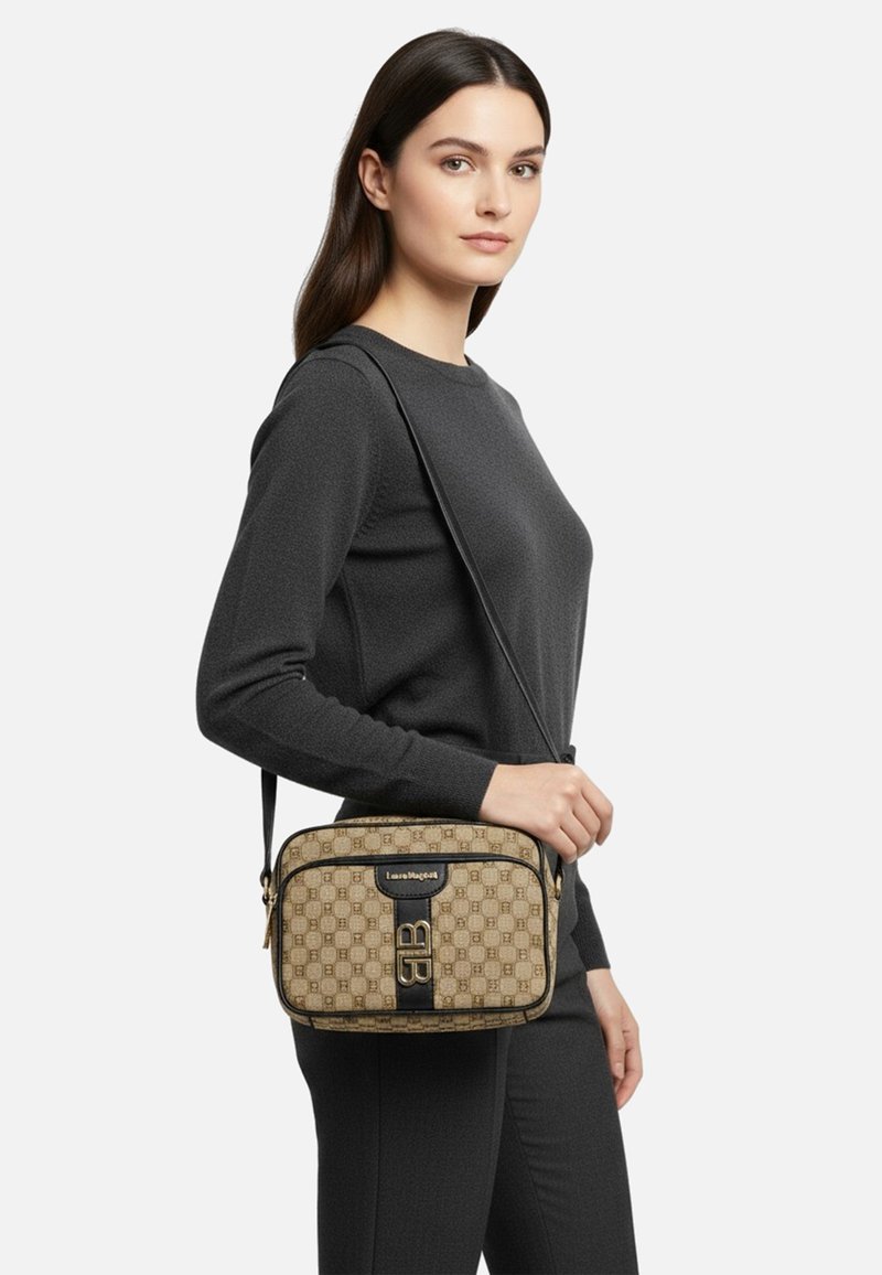 Borsa a tracolla color cuoio con motivo geometrico, dettagli neri, texture liscia e dettaglio con logo. Indossata da una modella con un outfit scuro.