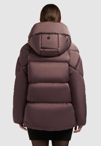 Kvinde med brunt hår iført en polstret, kviltet mauve vinterjakke med stor hætte, set bagfra mod en ensfarvet baggrund.