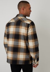 Karierte Flanellhemden in Grautönen, Schwarz und Beige. Mit Kragen, langen Ärmeln und Knopfmanschetten aus strukturiertem Stoff.