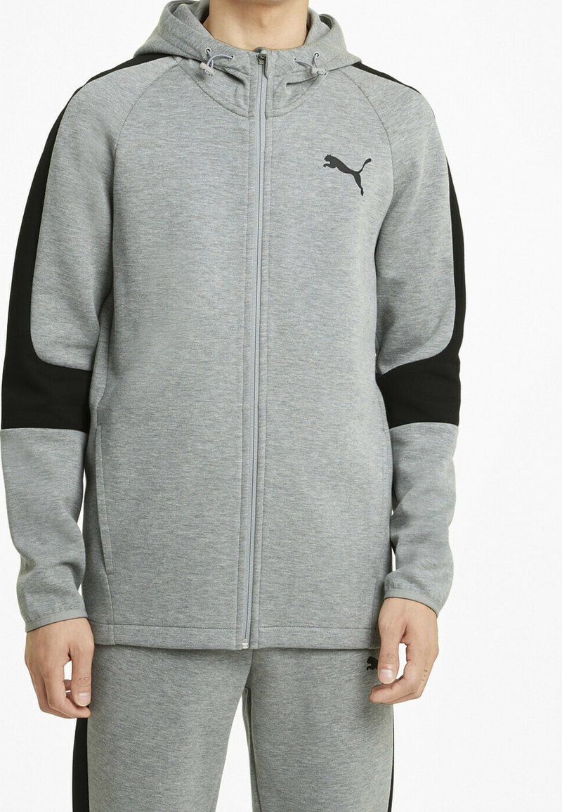 Sudadera con cremallera gris con acentos negros, hecha de una tela suave y texturizada. Cuenta con capucha, bolsillos laterales y un pequeño logotipo negro en el pecho.