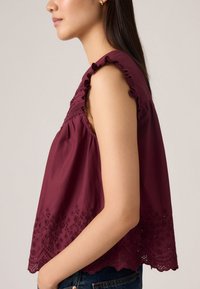 Top senza maniche color bordeaux con spalline arricciate, dettagli floreali ricamati all'orlo, tessuto morbido e vestibilità comoda.