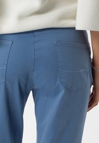 Vaaleansiniset housut, jotka on valmistettu sileästä kankaasta, joissa on kaksi takataskua ja suora leikkuu, yhdistettynä kermaiseen teksturoituun neulepaitaan.