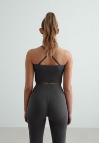 Sötétszürke, bordás sportmelltartó és magas derekú leggings, amelyek cropped kialakítással rendelkeznek, vízszintes varrással és minimális apró kiegészítőkkel.